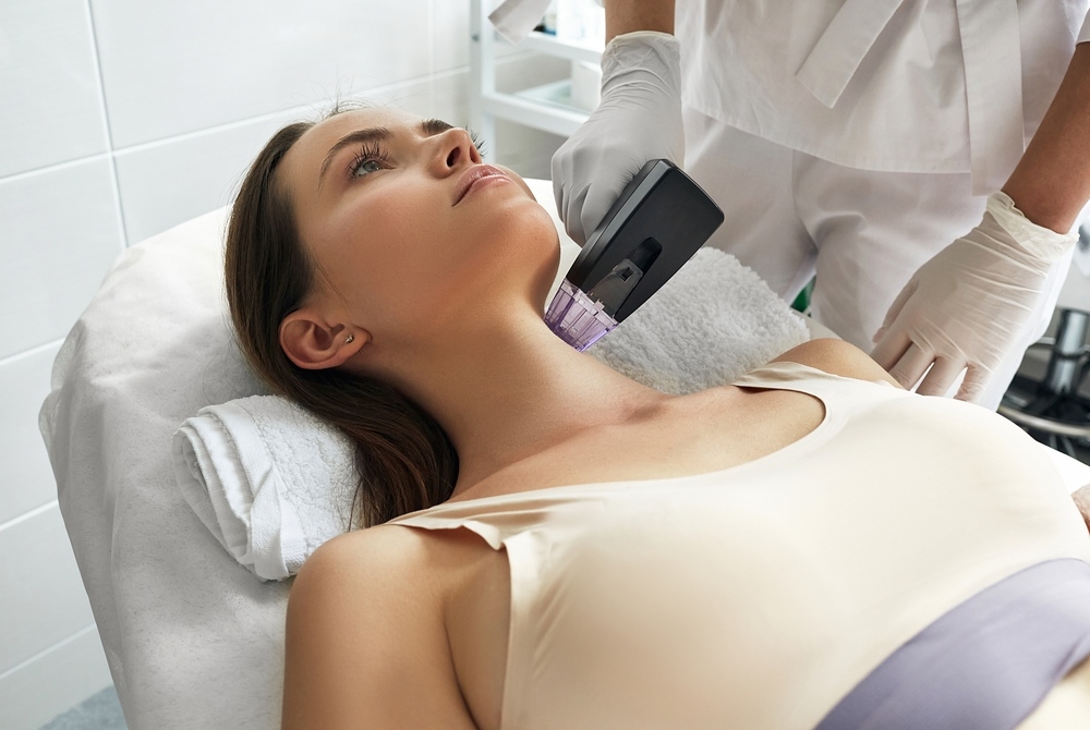 Woman receiving radiofrequency skin tightening treatment on neck and jawline at a medical spa