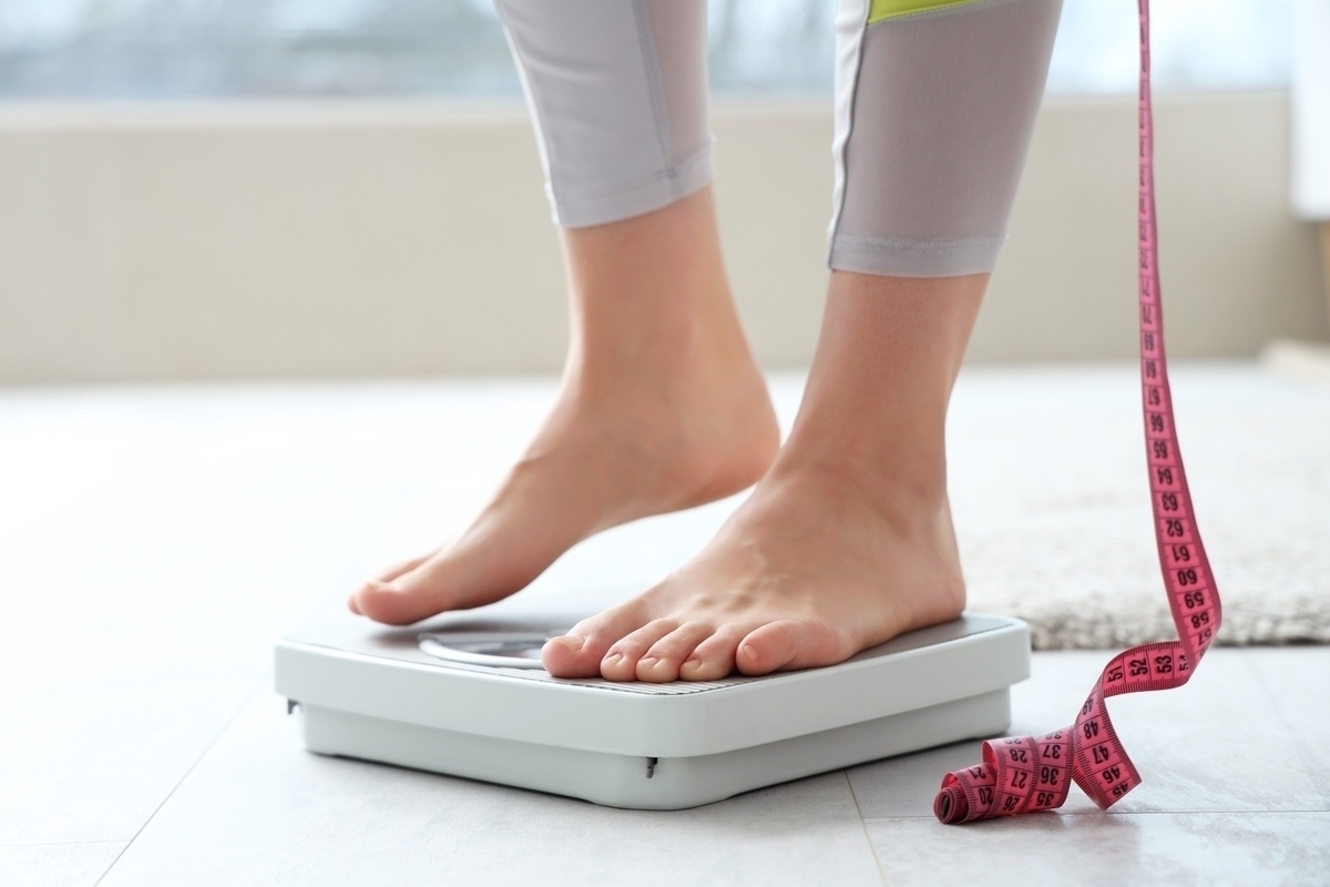 Person stepping on a scale with a measuring tape tracking medical weight loss results during a supervised treatment program