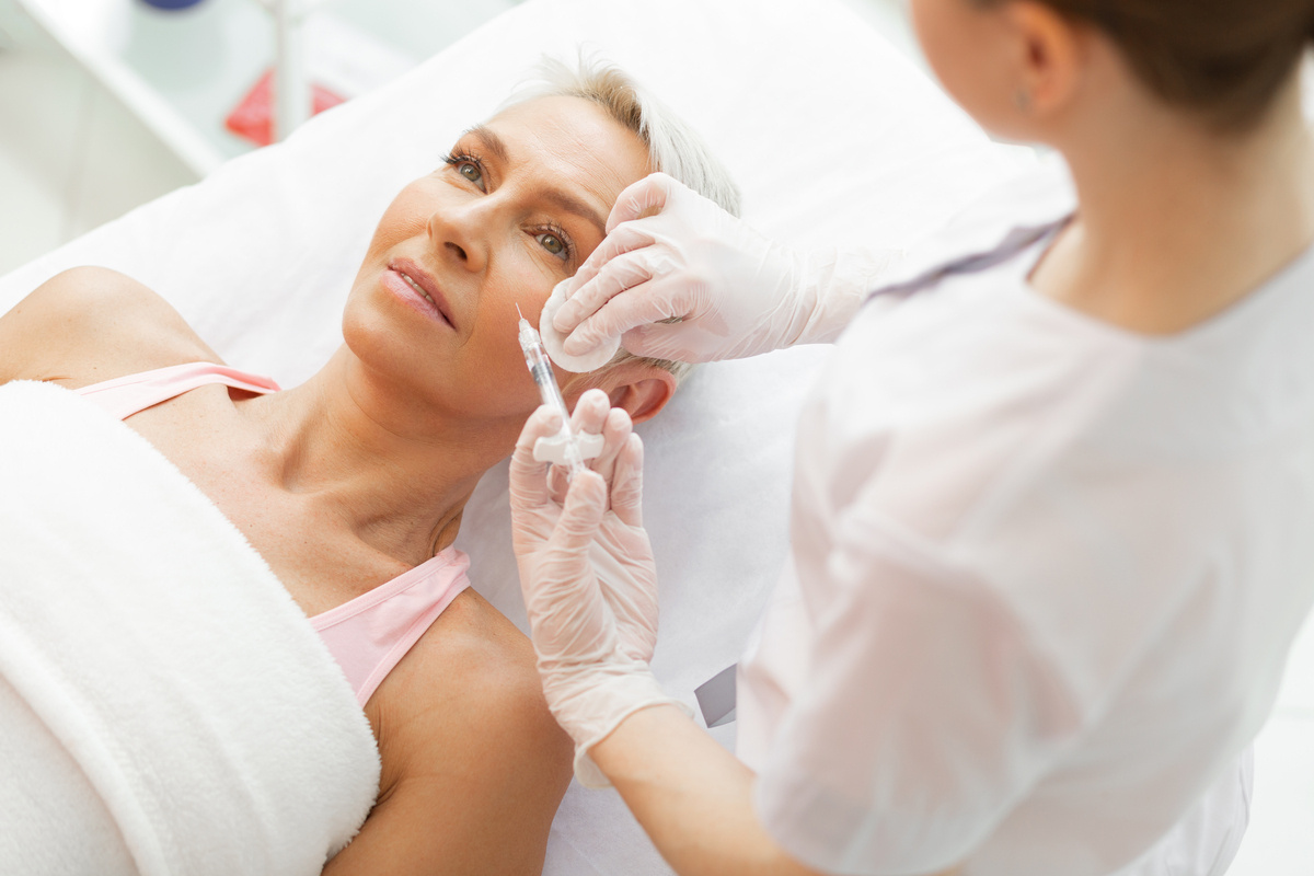 Mature woman lying on a treatment bed receiving a facial injection during a first time Botox appointment at a medical aesthetics clinic