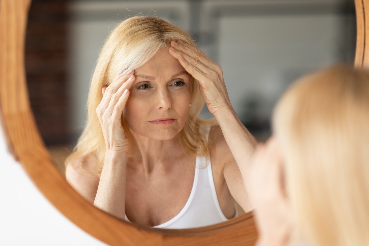 Mature woman examining her forehead and brow in a mirror to assess how long does Botox last after a wrinkle relaxer treatment